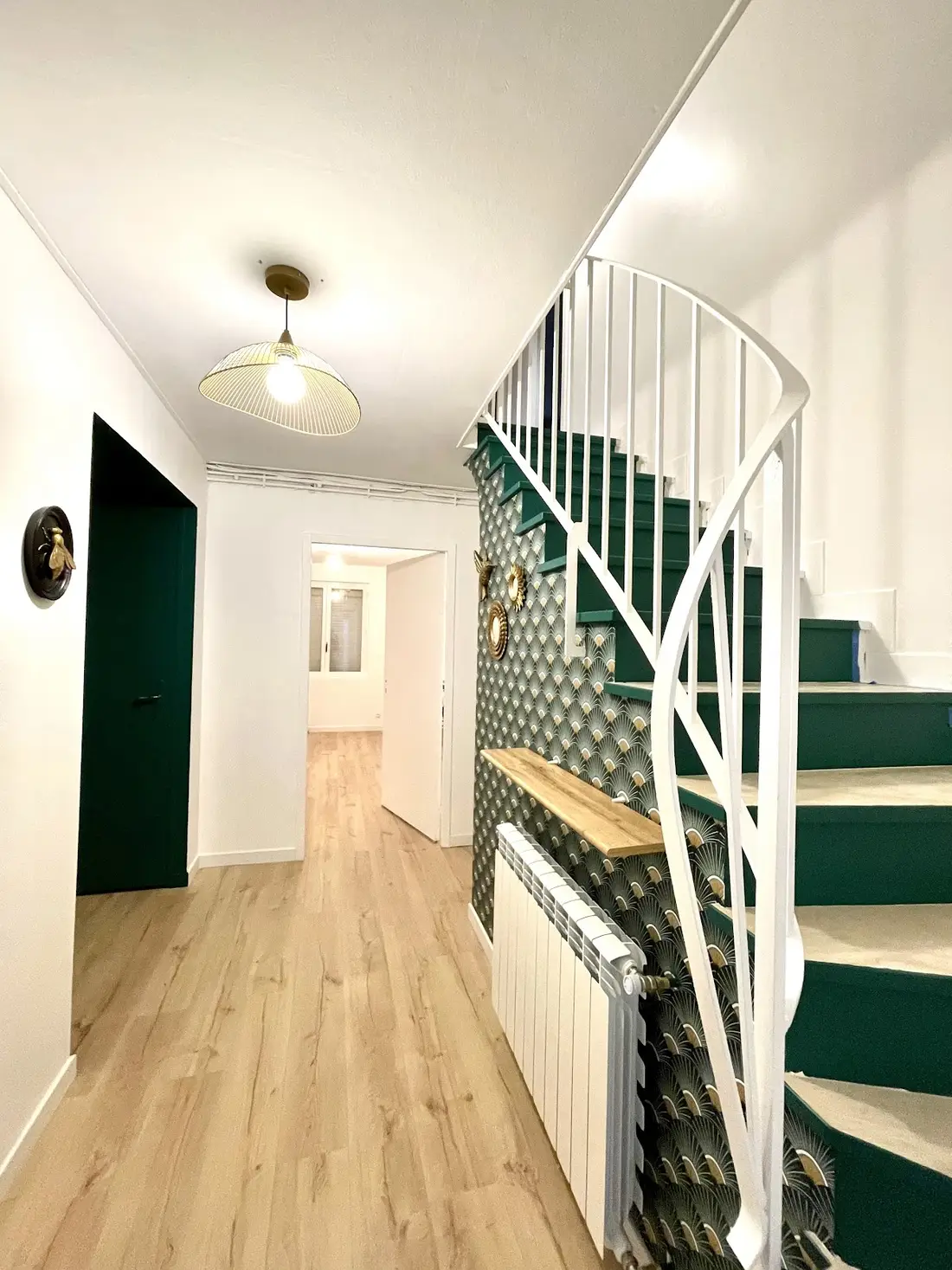 Le hall du cabinet : un escalier vert foncé, un papier peint à motifs d'éventails vert et or, un parquet clair